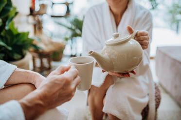 Nahaufnahme eines älteren Paares im Bademantel, das sich einen heißen Tee einschenkt, ruhige und gemütliche Atmosphäre. - HPIF11503