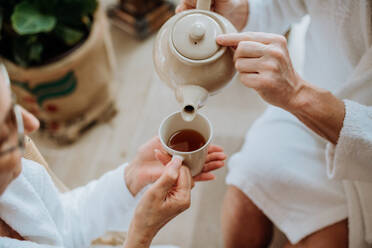 Nahaufnahme eines älteren Paares im Bademantel, das sich einen heißen Tee einschenkt, ruhige und gemütliche Atmosphäre. - HPIF11512