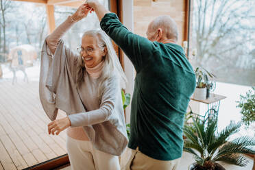 Verliebtes älteres Paar tanzt zusammen in ihrem schönen modernen Wohnzimmer. - HPIF11524