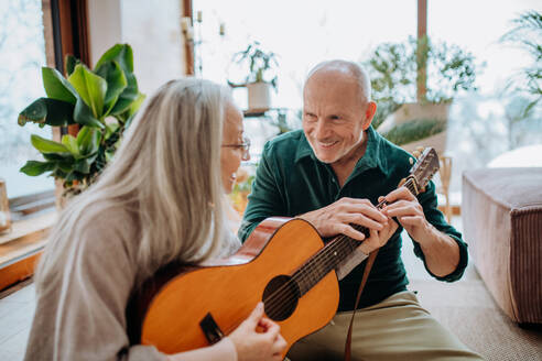 Ein älteres Paar spielt auf einer Gitarre, sitzt in einem gemütlichen Wohnzimmer und genießt den Herbsttag. - HPIF11529
