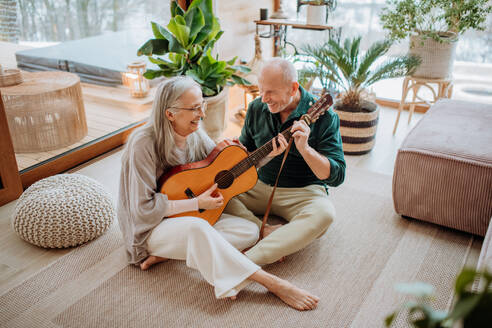 Ein älteres Paar spielt auf einer Gitarre, sitzt in einem gemütlichen Wohnzimmer und genießt den Herbsttag. - HPIF11530