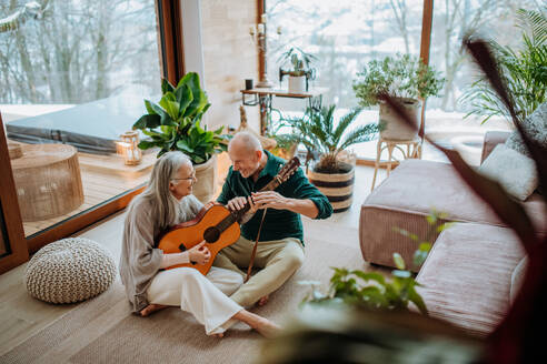 Ein älteres Paar spielt auf einer Gitarre, sitzt in einem gemütlichen Wohnzimmer und genießt den Herbsttag. - HPIF11531