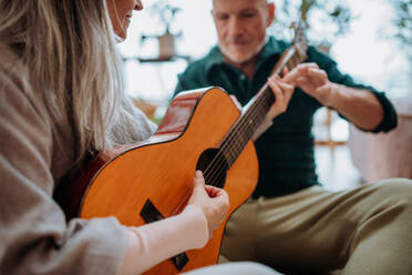 Ein älteres Paar spielt auf einer Gitarre, sitzt in einem gemütlichen Wohnzimmer und genießt den Herbsttag. - HPIF11532