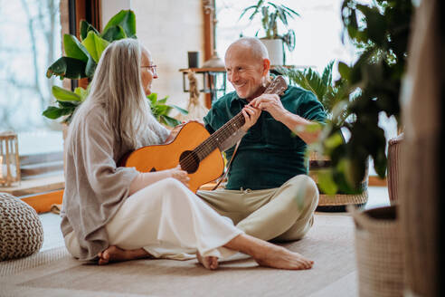 Ein älteres Paar spielt auf einer Gitarre, sitzt in einem gemütlichen Wohnzimmer und genießt den Herbsttag. - HPIF11533