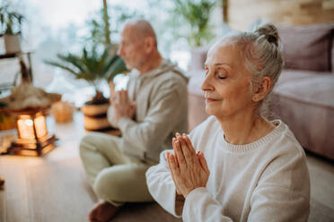 Senior couple meditating together in their living room during a cold autumn day. - HPIF11534