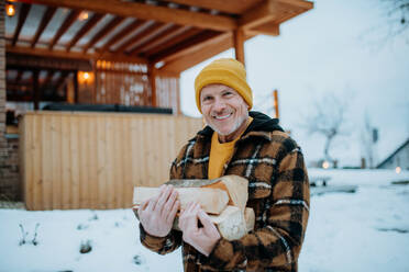 Ein älterer Mann trägt Holzscheite für die Zubereitung eines Feuers im Freien an einem Wintertag. - HPIF11542