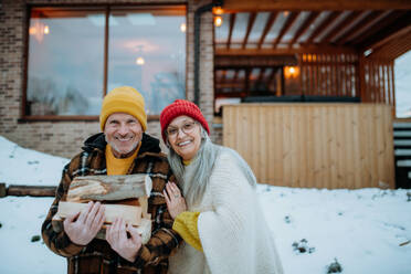 Porträt eines älteren Ehepaars, das Holzscheite trägt und ein Feuer im Freien vorbereitet, an einem Wintertag. - HPIF11543
