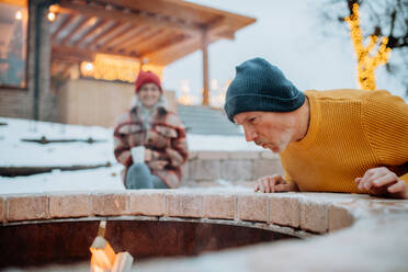 Älteres Ehepaar, das an einem Winterabend gemeinsam an einer Feuerstelle im Freien sitzt und heizt. - HPIF11552