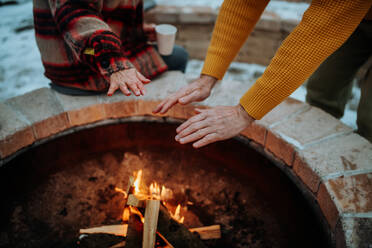 Senior couple sitting and heating together at outdoor fireplace during winter evening. - HPIF11553