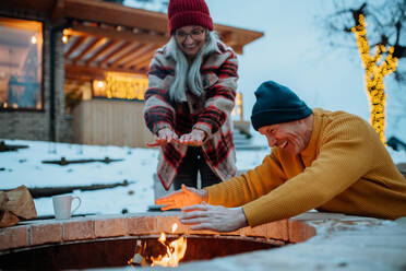 Senior couple sitting and heating together at outdoor fireplace during winter evening. - HPIF11554