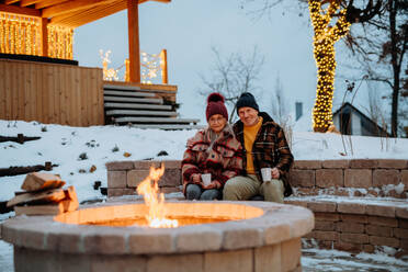 Senior couple sitting and heating together at outdoor fireplace during winter evening. - HPIF11556