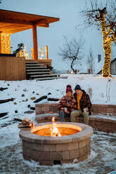 Senior couple sitting and heating together at outdoor fireplace during winter evening. - HPIF11557