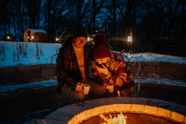 Älteres Ehepaar, das an einem Winterabend gemeinsam an einer Feuerstelle im Freien sitzt und heizt. - HPIF11558