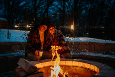 Älteres Ehepaar, das an einem Winterabend gemeinsam an einer Feuerstelle im Freien sitzt und heizt. - HPIF11559