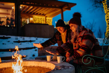 Senior couple sitting and heating together at outdoor fireplace during winter evening. - HPIF11560