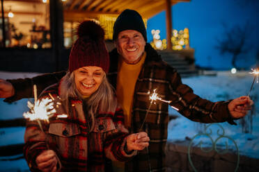 Glückliches älteres Paar, das das neue Jahr mit Wunderkerzen feiert und den Winterabend genießt. - HPIF11563