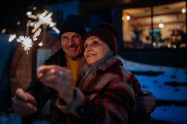 Glückliches älteres Paar, das das neue Jahr mit Wunderkerzen feiert und den Winterabend genießt. - HPIF11566