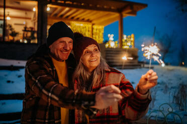 Glückliches älteres Paar, das das neue Jahr mit Wunderkerzen feiert und den Winterabend genießt. - HPIF11567