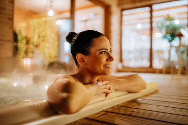 Junge Frau genießt an einem kalten Winterabend eine Badewanne auf ihrer Terrasse. - HPIF11570