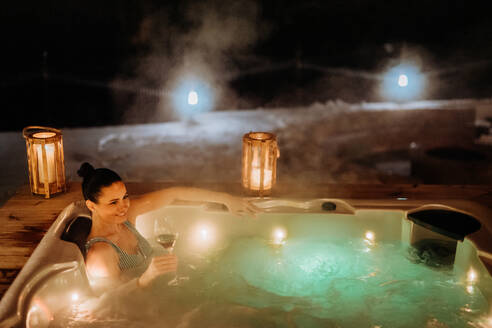 Junge Frau genießt an einem kalten Winterabend eine Badewanne auf ihrer Terrasse. - HPIF11584