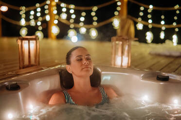 Junge Frau genießt an einem kalten Winterabend eine Badewanne auf ihrer Terrasse. - HPIF11585
