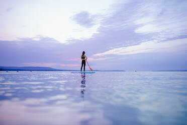 A young beautiful girl surfer paddling on surfboard on the lake at sunrise - HPIF11591