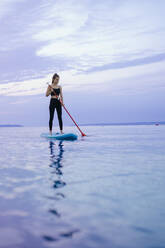 A young beautiful girl surfer paddling on surfboard on the lake at sunrise - HPIF11592