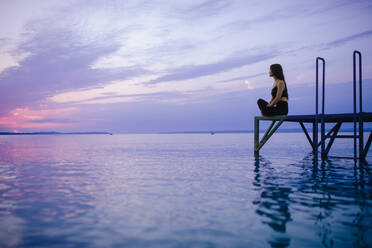 A young beautiful sportive girl meditating at early morning by the lake. - HPIF11595