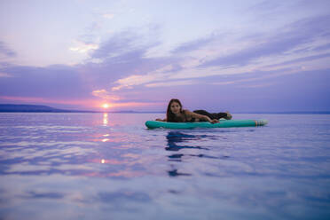 A young beautiful girl surfer paddling on surfboard on the lake at sunrise - HPIF11596