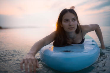 A young beautiful girl surfer paddling on surfboard on the lake at sunrise - HPIF11597