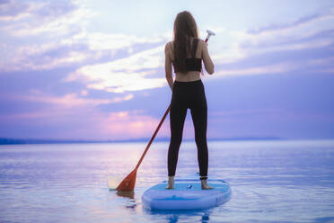 A young girl surfer paddling on surfboard on the lake at sunrise. - HPIF11601