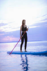 A young beautiful girl surfer paddling on surfboard on the lake at sunrise - HPIF11603
