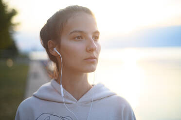Ein junges, schönes, sportliches Mädchen, das bei Sonnenaufgang am See Musik hört. - HPIF11606