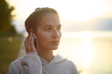 A young beautiful sportive girl listening to music at sunrise by the lake. - HPIF11607