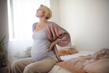 Tired pregnant woman sitting on her bed and resting. - HPIF11618