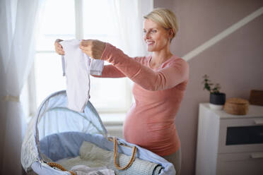 Glückliche schwangere Frau mit Blick auf kleine Babykleidung. - HPIF11627