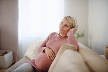 Pregnant woman sitting on a sofa, listening music and enjoying time for herself. - HPIF11632