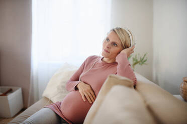 Schwangere Frau sitzt auf einem Sofa, hört Musik und genießt die Zeit für sich selbst. - HPIF11632