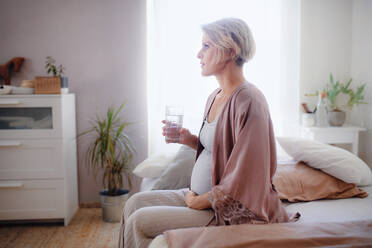 Pregnant woman drinking water in a bed, at morning. Healthy lifestyle and morning routine in pregnancy, concpet. - HPIF11638