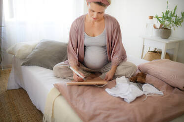 Hochformatige Ansicht einer schwangeren Frau, die ihren Geburtstermin in den Kalender einträgt. - HPIF11652
