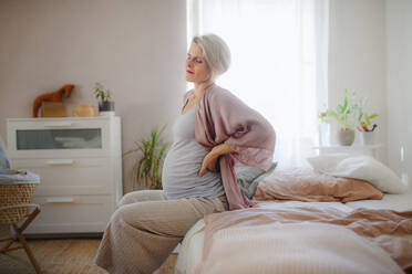 Tired pregnant woman sitting on her bed and resting. - HPIF11653