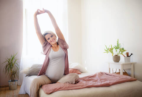 Schwangere Frau sitzt auf einem Bett und streckt sich. - HPIF11655