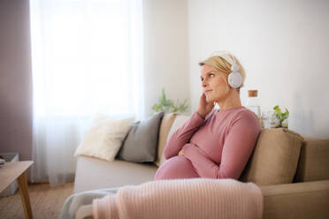 Pregnant woman sitting in a bed, listening music and enjoying time for herself. - HPIF11675