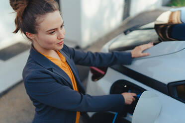 Junge Frau lädt ihr Auto zu Hause auf, nachhaltiges und wirtschaftliches Verkehrskonzept. - HPIF11706