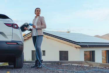 Junge Frau lädt Elektroauto zu Hause auf, nachhaltiges und wirtschaftliches Verkehrskonzept. - HPIF11719