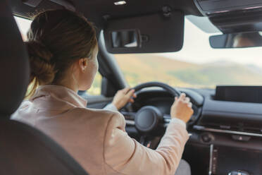 Rückansicht einer jungen Frau, die ein Elektroauto fährt. - HPIF11724