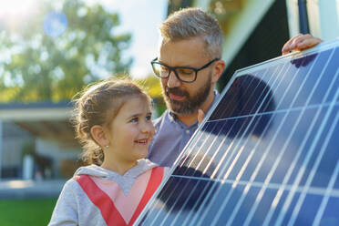 Vater mit seiner kleinen Tochter in der Nähe des Hauses mit Sonnenkollektoren. Alternative Energie, Ressourcenschonung und nachhaltiger Lebensstil. - HPIF11747