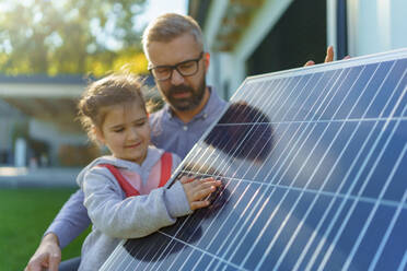 Ein Vater zeigt seiner kleinen Tochter die Funktionsweise von Photovoltaikmodulen und erklärt ihr, wie alternative Energie, Ressourcenschonung und nachhaltiger Lebensstil funktionieren. - HPIF11748