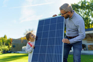 Vater mit seiner kleinen Tochter in der Nähe des Hauses mit Sonnenkollektoren. Alternative Energie, Ressourcenschonung und nachhaltiger Lebensstil. - HPIF11749