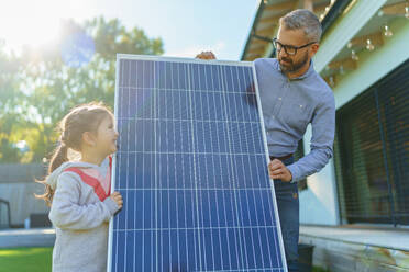 Father with his little daughter near the house with solar panels. Alternative energy, saving resources and sustainable lifestyle concept. - HPIF11752